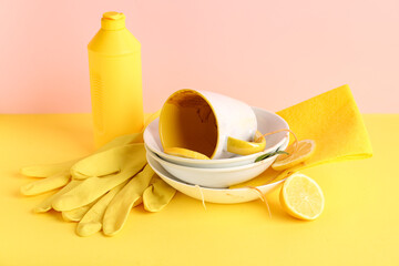 Dirty dishes with rubber gloves and detergent on color background