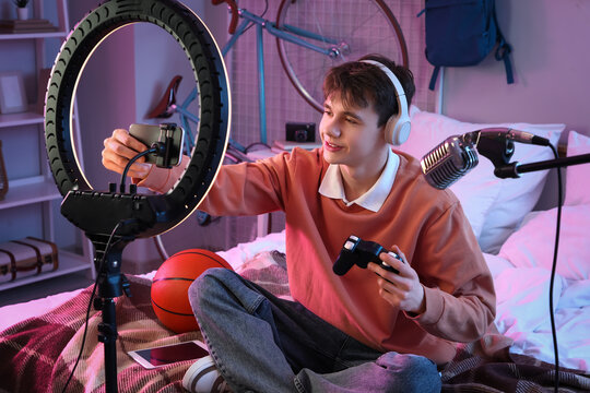 Teenage blogger with game pad recording video in bedroom