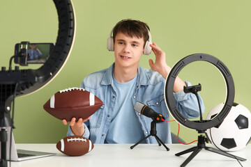 Teenage sports blogger in headphones with rugby ball recording video at table on green background
