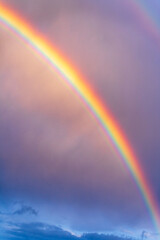 Vivid rainbow arcs across the dramatic twilight sky, casting a magical spectrum of colors through soft pastel clouds just after the rain.