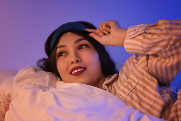 Beautiful young woman with sleep mask lying in bed at night