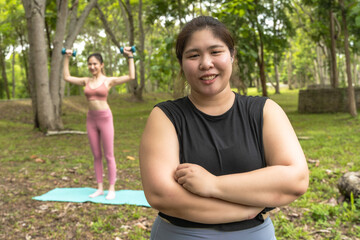 Asian fat sportswoman doing exercise yoga in park with female trainer