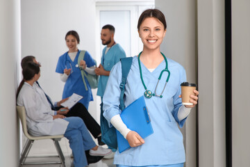 Female medical intern with coffee cup and clipboard in hall