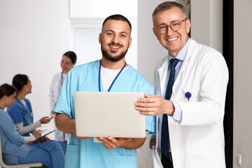Male medical intern and doctor with laptop in hall
