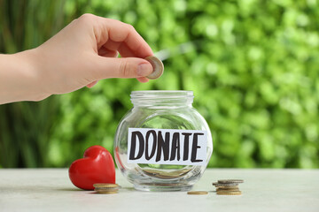 Hand, jar with word DONATE, coins and red heart on table outdoors