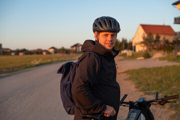 Man in helmet with backpack on bike in warm sunset light.