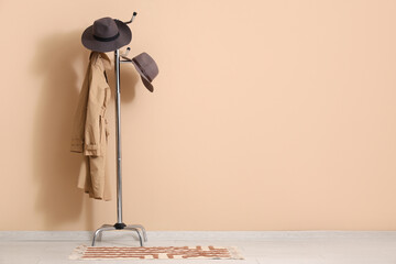 Rack with coat and felt hats near beige wall