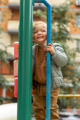 Obraz premium Vertical portrait of a small red-haired boy who looks over the fence of a playground in the city. Outdoor games