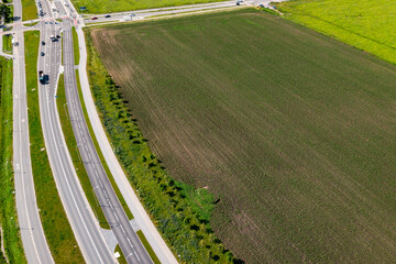 Urban bypass road running along large plowed field and green belt with cars and cycle lanes visible