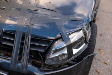 Fototapeta premium damaged black car after crash, hood taped with duct tape, scratched surface, Urban accident detail, Emergency car repair