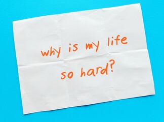 Paper on blue background with text written - Why is my life so hard? - emotional feeling with doubt when life are bad - overwhelmed with obstacles and hardship - Struggling with life challenges