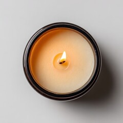 A top-down view of a lit candle in a dark container, set against a light background, exuding warmth and ambiance.