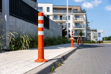 Close-up of orange flexible traffic bollard installed on sidewalk in front of modern apartment building