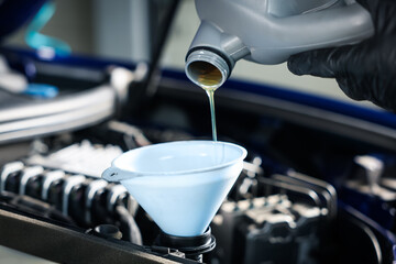 Worker pouring motor oil from canister into car engine, closeup