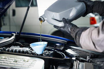 Worker pouring motor oil from canister into car engine, closeup