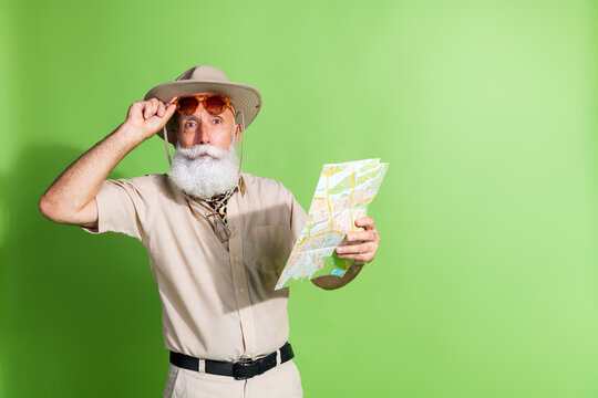 Photo of surprise old man touch sunglass hold map observe finding place isolated green color background