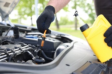 Worker checking motor oil level in car with dipstick, closeup