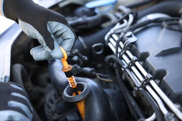 Worker checking motor oil level in car with dipstick, closeup