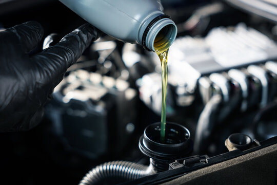 Worker pouring motor oil from bottle into car engine, closeup