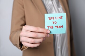 Human resources manager holding sticky note with word Welcome To The Team on grey background,...