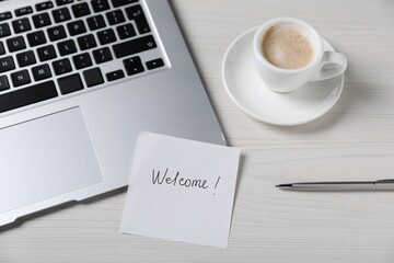Paper note with word Welcome, laptop, cup of coffee and pen on light wooden table, above view