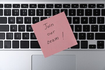Sticky note with phrase Join Our Team on laptop, top view