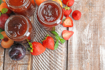 Different jams in jars and ingredients on wooden table, flat lay. Space for text