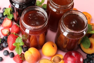Different jams in jars and ingredients on light pink background, closeup
