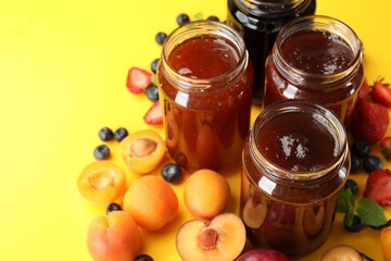 Different jams in jars and ingredients on yellow background, closeup