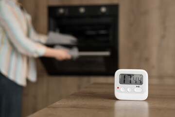 Kitchen timer on table against woman baking in room, closeup