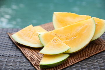 Pieces of ripe yellow watermelon on wicker table near swimming pool, closeup
