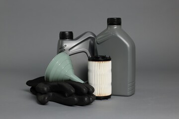 Motor oil in plastic canisters, filter, gloves and funnel on grey background