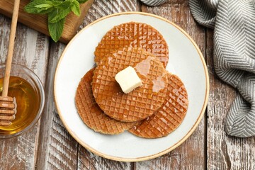 Tasty Dutch waffles (stroopwafels) with honey and butter cube on wooden table, flat lay