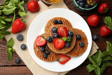 Tasty Dutch waffles (stroopwafels) with honey, berries and mint on wooden table, flat lay