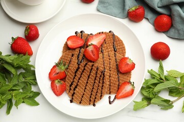 Tasty Dutch waffles (stroopwafels) with strawberries, mint and chocolate sauce on white marble table, flat lay