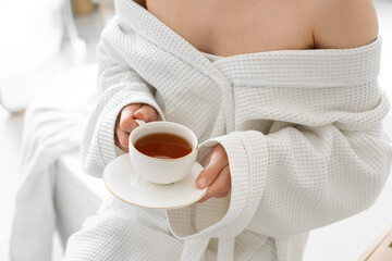 Young woman in waffle robe with cup of tea at home, closeup
