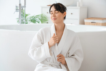 Young woman in waffle robe near bathtub at home