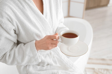 Young woman in soft bathrobe with cup of tea at home