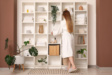 Young woman with towels on shelf unit in bathroom, back view