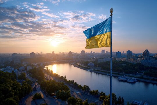 Ukraines flag waves over Kyiv with the Dnieper River and city skyline visible at sunrise