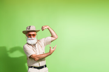 Elderly man in fashionable safari outfit posing confidently against a green background, showcasing his adventurous spirit and summer style.