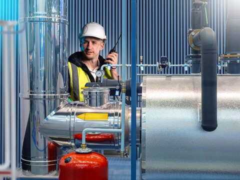 Man in industrial brewery shop. Production worker with walkie-talkie. Brewery worker behind steel tanks. Brewery industry specialist. Man engineer inside plant. Food industry career