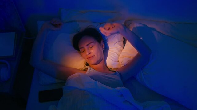 High angle shot of brunette sleepy woman stretching while lying in bed and trying to wake up in morning
