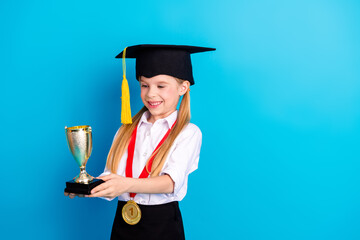 Cute female student celebrating academic achievement with trophy and medal against vibrant blue...