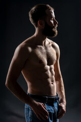 Shirtless fit man with beard posing in shadow on dark background. Concept of strength, masculinity, and body confidence in modern portrait photography