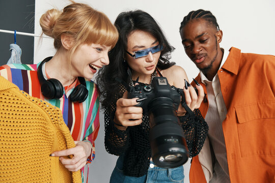 Young adult woman working with colleagues and friends in a casual workplace, socializing while reviewing photos on a DSLR camera with Gen Z coworkers.