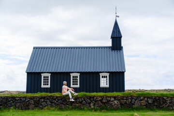 Fototapeta premium Charming black church in Iceland with a visitor contemplating nature and tranquility