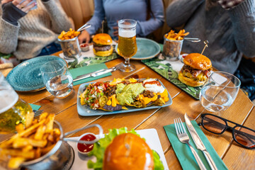 Friends enjoying nachos, burgers, french fries, and beer at restaurant table