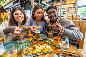 Happy multi ethnic friends eating nachos, burgers and fries at restaurant