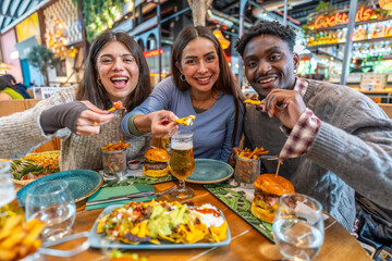 Happy friends eating nachos, burgers and fries at restaurant
